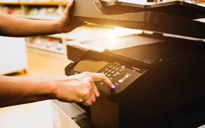 Close-up of a hand pressing the copy button on an office photocopier